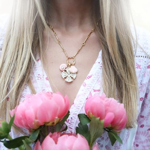 Detail of a gold necklace featuring a pink shell and white enamel clover pendant on model