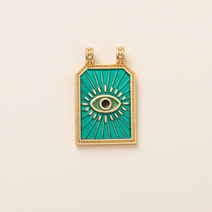 Macro detail of tarot style gold pendant featuring green enamel and evil eye motif