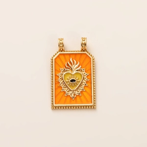 Detail of a tarot-style gold pendant with orange enamel heart and evil eye motif