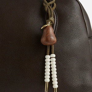 Detail of woven rope charm with wooden pear pendant and white beads on leather bag