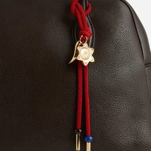 Close-up of red braided rope bag charm with gold charms on dark brown lychee leather