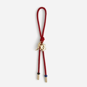 Detail of red braided rope accessory with gold horn and star pendants for handbags
