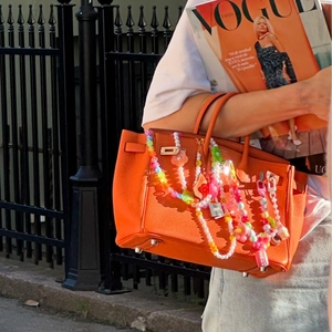 Bunte Perlen-Taschenkette mit Herz- und Blumenanhängern an einer orangen Handtasche