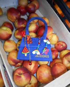 Detail einer blauen Wildledertasche mit bunten Anhängern in einem Korb voller Pfirsiche