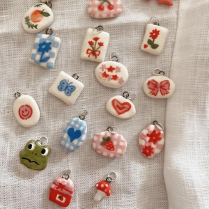 Bunte Keramik-Anhänger mit Obst- und Blumenmustern auf weißem Leinenhintergrund