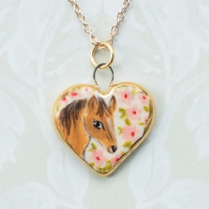 Dettaglio macro del ciondolo a cuore con motivo a cavallo dipinto a mano e bordo oro