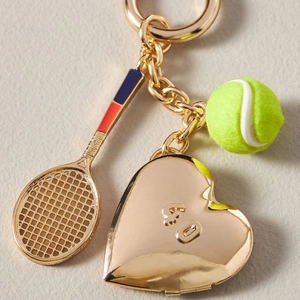 Porte-clés raquette de tennis dorée avec balle verte et breloque coeur gravée sur fond beige