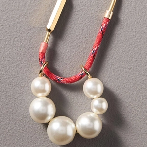 Détail macro du collier en corde tressée avec maillons dorés et perles blanches dégradées