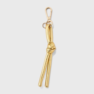 Detail view of a luxury gold leather knot keychain with tassels and metallic spring clip