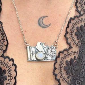 Dettaglio di una collana vintage in argento con ciondolo a libro e corvo e pietra di luna