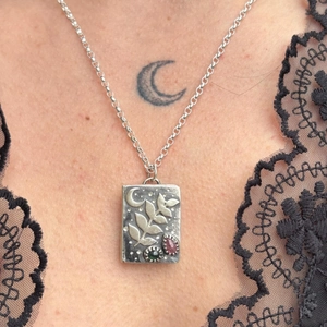 Dettaglio di pendente vintage in argento con rilievo di luna e foglia su catena fine