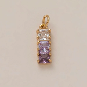 Dettaglio macro di un ciondolo placcato oro con tre cristalli quadrati viola e trasparenti