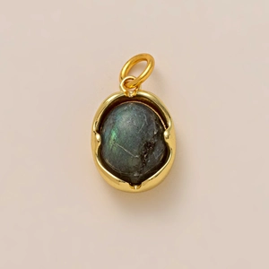 Macro view of oval labradorite pendant with golden bezel and green flash on pink background