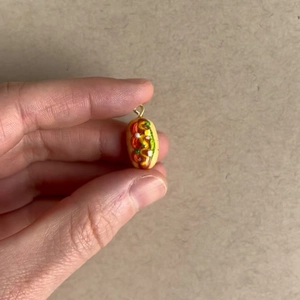 Gros plan d'un pendentif hot-dog miniature sur un doigt pour montrer sa taille minuscule