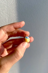 Gros plan d'un pendentif globe vintage tenu entre les doigts avec détails de la carte du monde