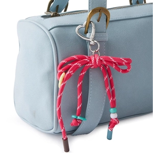 Red woven bow bag charm with silver heart clip on a light blue fashion handbag