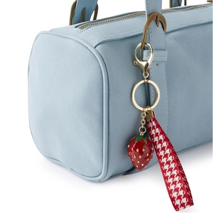 Detail of strawberry keychain with red resin pendant and houndstooth ribbon on a blue bag
