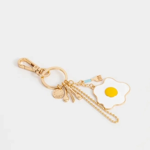 Détail d'un porte-clés doré avec pendentif œuf au plat en émail et mini breloques couverts
