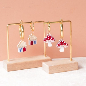 Detailed view of handmade house and mushroom gold earrings on a display stand