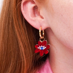 Close-up of red flower earring with evil eye motif and gold ring on woman's ear