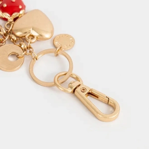 Détail macro du porte-clés doré avec charms fraise et cœur pour sacs à main