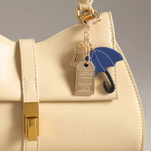Detail van een beige leren tas met Londen thema hangers, blauwe paraplu en rode bus