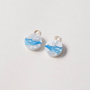 Close-up of circular 18K gold-plated jade pendants with blue wave patterns on white base