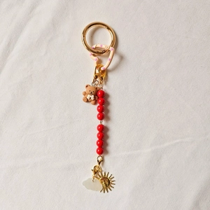 Detailed view of a gold keychain featuring a brown bear, red beads, and sun charms