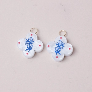 Detail of 18K gold clover pendants featuring delicate blue floral motifs on white resin