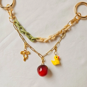 Detail of keychain with gold bow pendant, red bead, and yellow duck on textured background