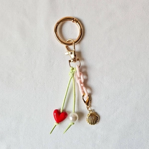 Detail of keychain with pink resin chain, shell pendant, and golden hardware on white fabric