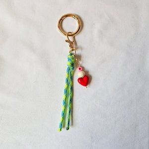 Detail of handmade keychain with red heart bead and blue-green braided cord on fabric