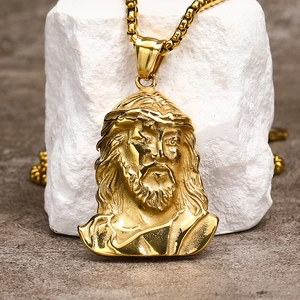 Close-up of golden Jesus pendant with thorn crown detail on box chain over white stone