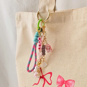 Colorful strawberry milk charm keychain with woven rope on a canvas tote bag
