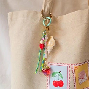 Handmade beaded keychain with strawberry and conch charms on a canvas bag handle
