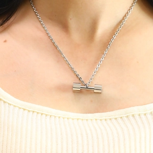 Close-up of a silver fitness dumbbell pendant on a metal chain worn by a model