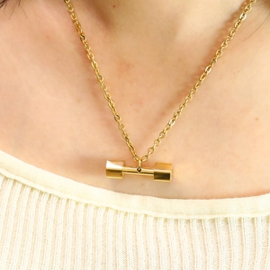 Golden dumbbell pendant necklace in stainless steel on a model with knitwear