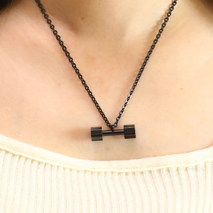 Close-up of black dumbbell pendant necklace worn by model over a yellow ribbed top
