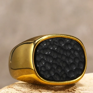 Detail eines goldenen Siegelrings mit schwarzer gehämmerter Einlage auf Holzbasis