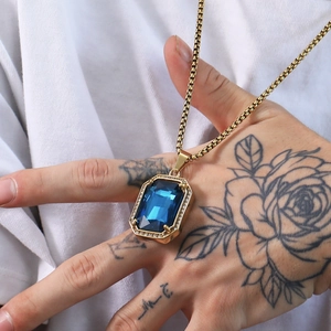 Detail showing square blue gemstone pendant with zircon halo on a gold woven chain
