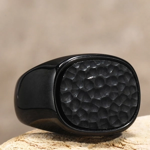Makroaufnahme eines schwarzen Titanrings für Herren mit Hammerschlag-Textur auf Stein