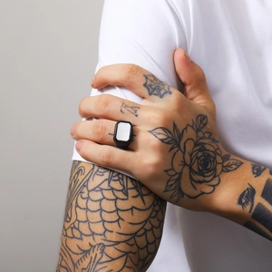 Close-up of matte black signet ring with white rectangular shell inlay on tattooed hand