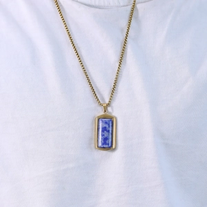 Detail van een gouden box chain ketting met blauwe lapis lazuli hanger op een wit shirt