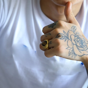 Dettaglio dell'anello punk dorato con pietra scura ovale su mano maschile tatuata