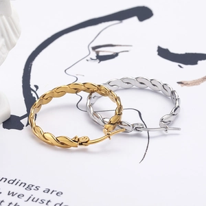 Moderne gedrehte Creolen in Gold und Silber vor minimalistischem Hintergrund mit Linienkunst
