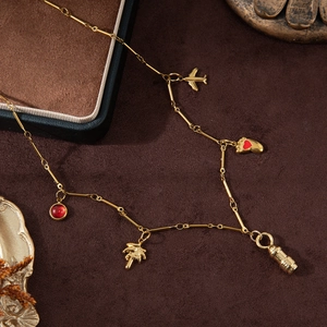 18K gold plated stainless steel necklace with bullet, airplane and heart charms on brown surface