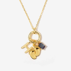 Detalle de collar de acero dorado de 18K con dije H, pies de bebé y gema color púrpura