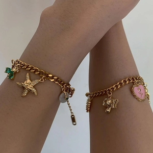 Dettaglio di bracciali a catena cubana dorati con ciondoli a cuore rosa e smeraldo al polso