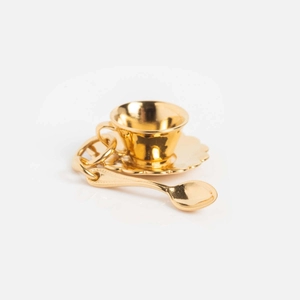 Détail d'un pendentif luxueux en forme de mini tasse à thé dorée avec soucoupe et cuillère