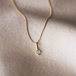 Gros plan d'un collier en chaîne dorée avec pendentif opale ronde sur soie champagne
